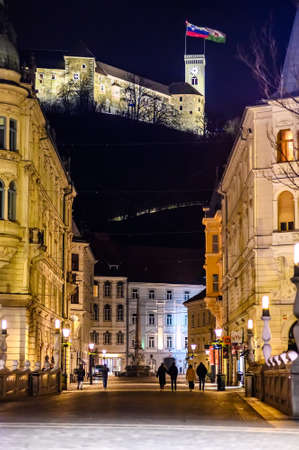 LJUBLJANA, SLOVENIA - FEBRUARY 15, 2022: Streets of Ljubljana with people and historic architecture at night with the Ljubljana castle in the backgroundのeditorial素材
