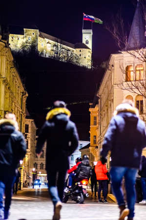 LJUBLJANA, SLOVENIA - FEBRUARY 15, 2022: Streets of Ljubljana with people and historic architecture at night with the Ljubljana castle in the backgroundのeditorial素材
