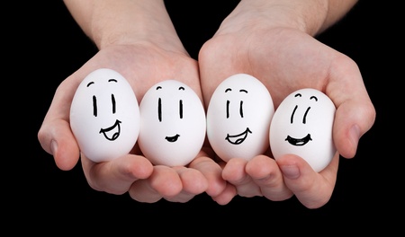 Hand holding cute eggs with funny face smileys on black background