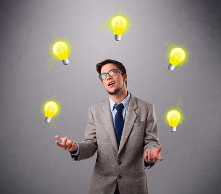 funny young man standing and juggling with light bulbsの写真素材