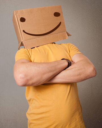 Young man standing and gesturing with a cardboard box on his head with smiley faceの写真素材