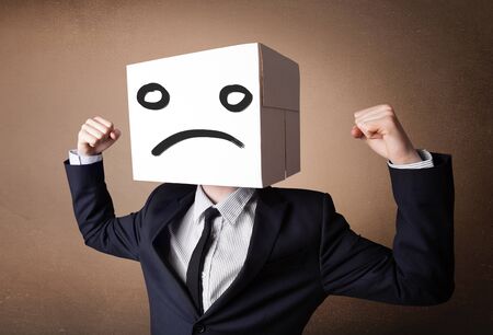 Businessman standing and gesturing with a cardboard box on his head with sad faceの写真素材