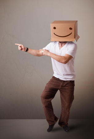 Young man standing and gesturing with a cardboard box on his head with smiley faceの写真素材