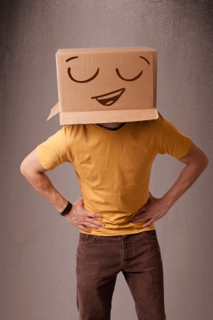 Young man standing and gesturing with a cardboard box on his head with smiley faceの写真素材