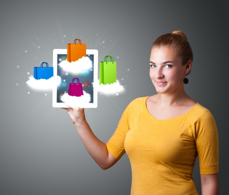 beautiful woman holding modern tablet with colorful shopping bags on cloudsの写真素材