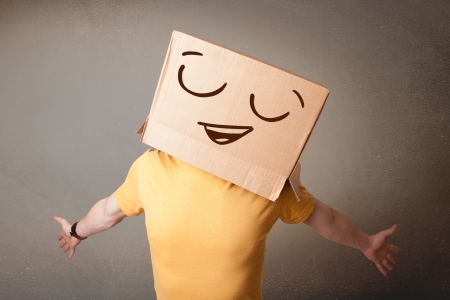 Young man standing and gesturing with a cardboard box on his head with smiley faceの写真素材