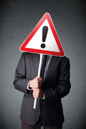 Businessman holding a red traffic triangle warning sign in front of his headの写真素材