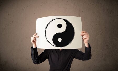 Businessman holding a paper with a yin-yang symbol on it in front of his headの写真素材