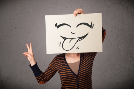 Young woman holding a paper with a cute smiley face on it in front of her headの写真素材