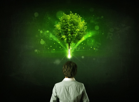 Young businessman standing with a glowing tree and letters above his headの写真素材