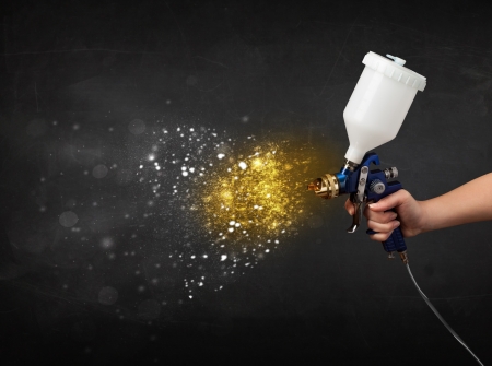Worker with airbrush painting with glowing golden paint and particlesの写真素材