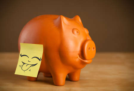 Drawn smiley face on a post-it note sticked on a piggy bankの写真素材