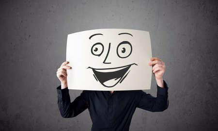 Young businessman holding a cardboard with a smiley face on it in front of his headの写真素材