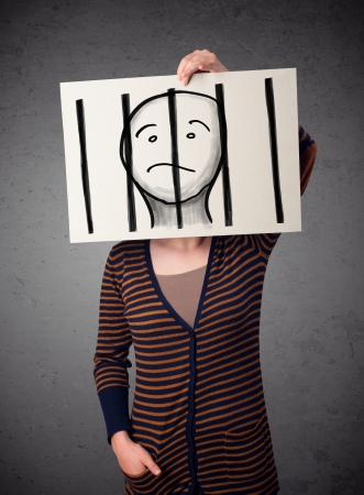 Woman holding a paper with a prisoner in jail behind the bars on it in front of her headの写真素材