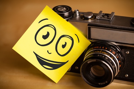 Drawn smiley face on a post-it note sticked on a photo cameraの写真素材
