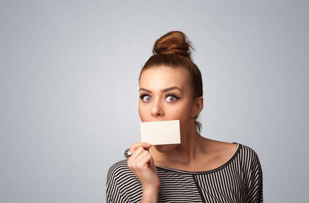 Cute girl holding white card at front of her lips with copy space on gradient backgroundの写真素材