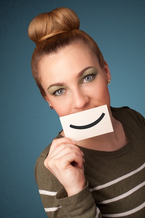 Happy pretty woman holding card with funny smiley on gradient backgroundの写真素材