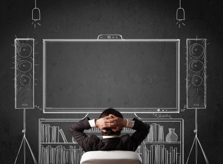 Young businessman sitting and enjoying home cinema system sketched on a chalkboard Young businessman sitting and enjoying home cinema system sketched on a chalkboard