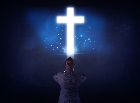 Young businessman standing and looking at a glowing cross above his head