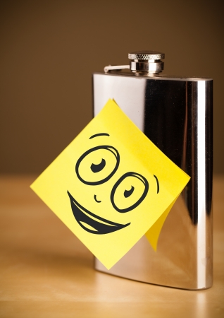 Drawn smiley face on a post-it note sticked on a hip flaskの写真素材