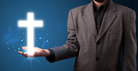 Young businessman holding a glowing cross in his handの写真素材
