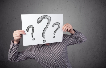 Businessman holding a paper with drawed question marks on it in front of his headの写真素材