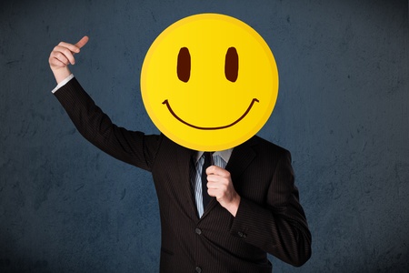 Businessman holding a yellow smiley face emoticon in front of his headの写真素材