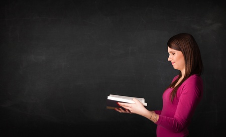 Young lady reading a book in front of a blackboard の写真素材
