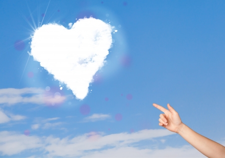 Hand pionting at white heart cloud on blue sky conceptの写真素材