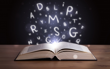 Open book with glowing letters flying out on wood deckの写真素材