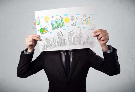 Businessman holding a paper in front of his head with charts and cityscape drawingの写真素材