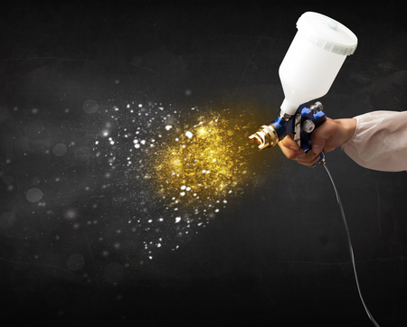 Worker with airbrush painting with glowing golden paint and particlesの写真素材