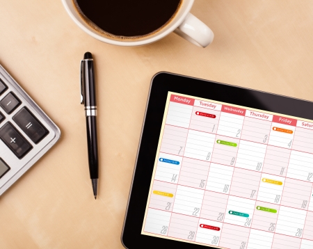 Workplace with tablet pc showing calendar and a cup of coffee on a wooden work table close-upの写真素材