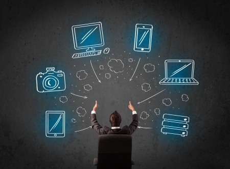 Young businessman in office chair sitting in front of a wall with glowing drawn multimedia icons above his headの写真素材