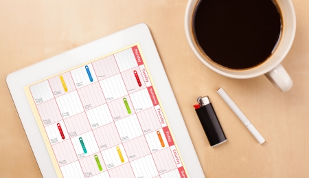 Workplace with tablet pc showing calendar and a cup of coffee on a wooden work table close-up