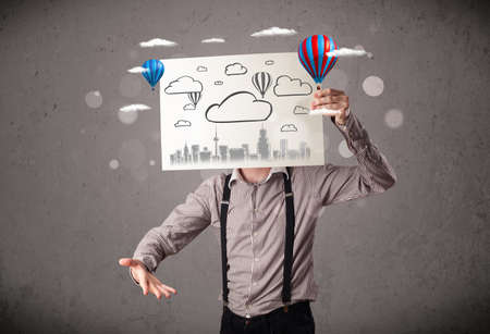 Businessman holding a cardboard in front of his head with cityscape and ballons drawingの写真素材
