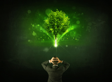Young businessman standing with a glowing tree and letters above his headの写真素材