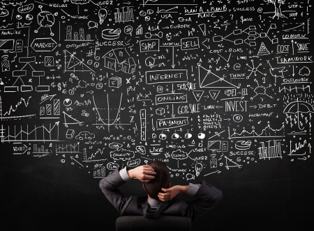 Young businessman sitting in office chair in front of a blackboard with sketched charts and signsの写真素材