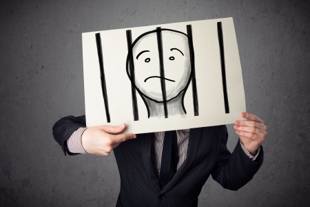 Businessman holding a paper with a prisoner in jail behind the bars on it in front of his headの写真素材