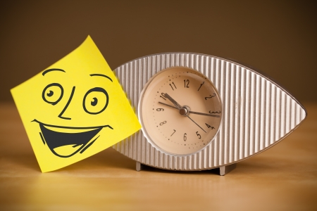Drawn smiley face on a post-it note sticked on a clockの写真素材