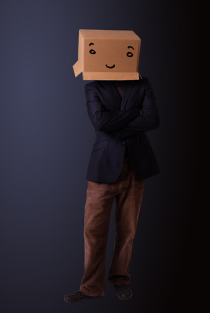 Young man standing and gesturing with a cardboard box on his head with smiley faceの写真素材
