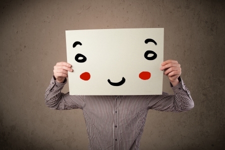 Young businessman holding a cardboard with a smiley face on it in front of his headの写真素材