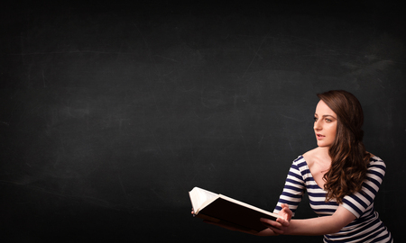 Young lady reading a book in front of a blackboard の写真素材
