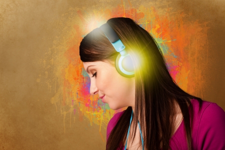 Pretty young woman with headphones listening to music in front of a painted wallの写真素材