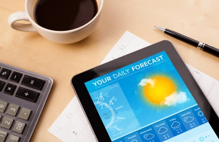 Workplace with tablet pc showing weather forecast and a cup of coffee on a wooden work table close-upの写真素材