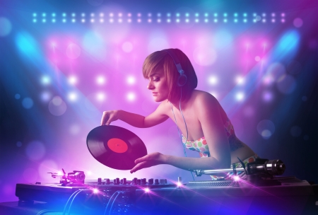 Pretty young disc jockey mixing music on turntables on stage with lights and stroboscopesの写真素材