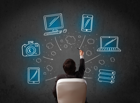 Young businessman in office chair sitting in front of a wall with glowing drawn multimedia icons above his headの写真素材