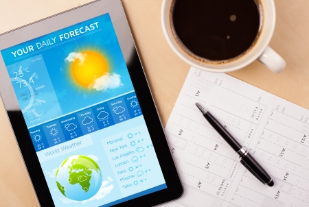 Workplace with tablet pc showing weather forecast and a cup of coffee on a wooden work table close-upの写真素材