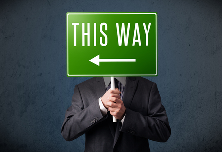 Businessman standing and holding a green direction sign in front of his headの写真素材