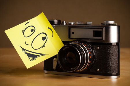 Drawn smiley face on a yellow note sticked on photo cameraの写真素材